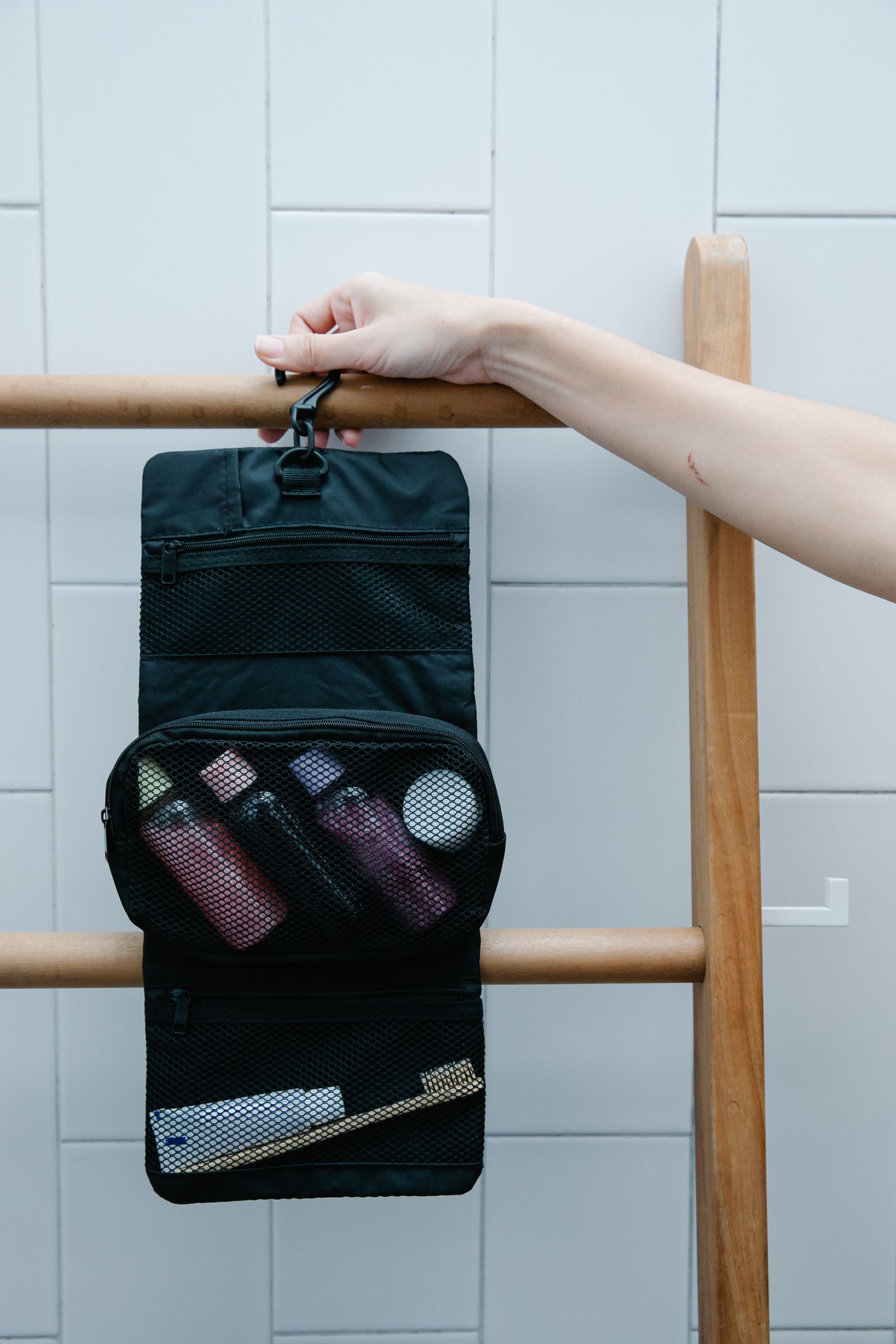 Travel toiletry bag with personal care essentials hanging from a wooden rack
